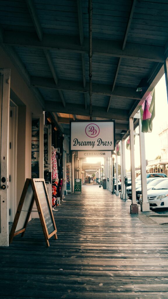 Explore a charming boutique street with a wooden walkway, featuring 'Dreamy Dress' and cozy shops.